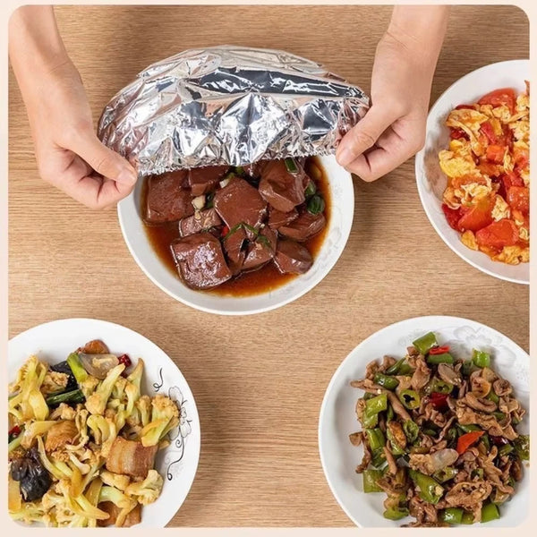 Hands holding a foil food bowl cover over a plate of cooked meat and scrambled eggs.