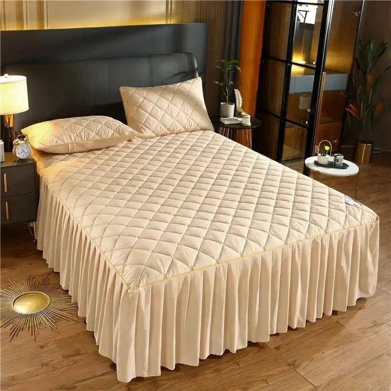 A beige quilted bed skirt with vertical pleats is displayed on a bed in a modern bedroom setting.