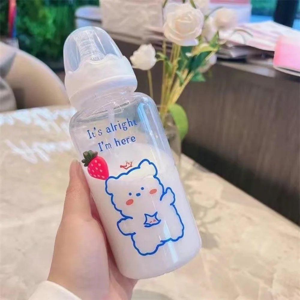 A hand holds a clear plastic water bottle with a strawberry bear design and a white cap on a table.