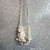 A light beige sequin accent chain shoulder bag hanging against a gray textured background.