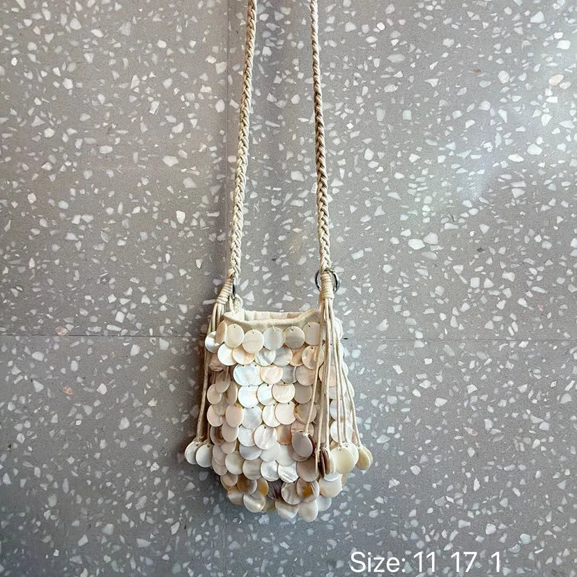 A light beige sequin accent chain shoulder bag hanging against a gray textured background.