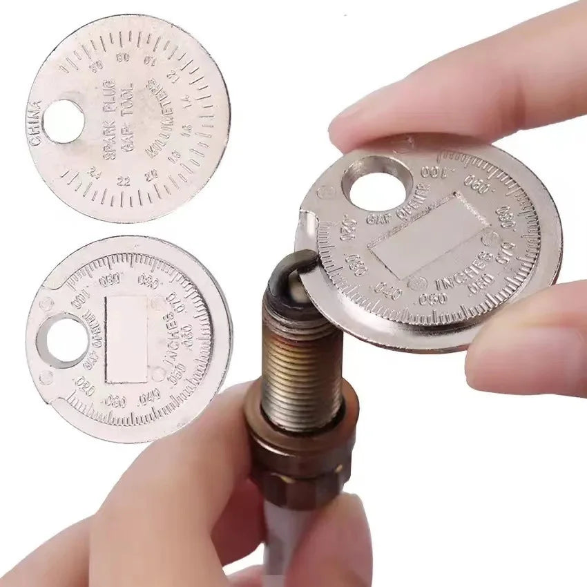 A hand holds a coin-type spark plug gap gauge with multiple measurement circles and a brass plug tip.