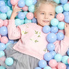 A smiling young girl is surrounded by a large collection of colorful plastic ball pit balls.