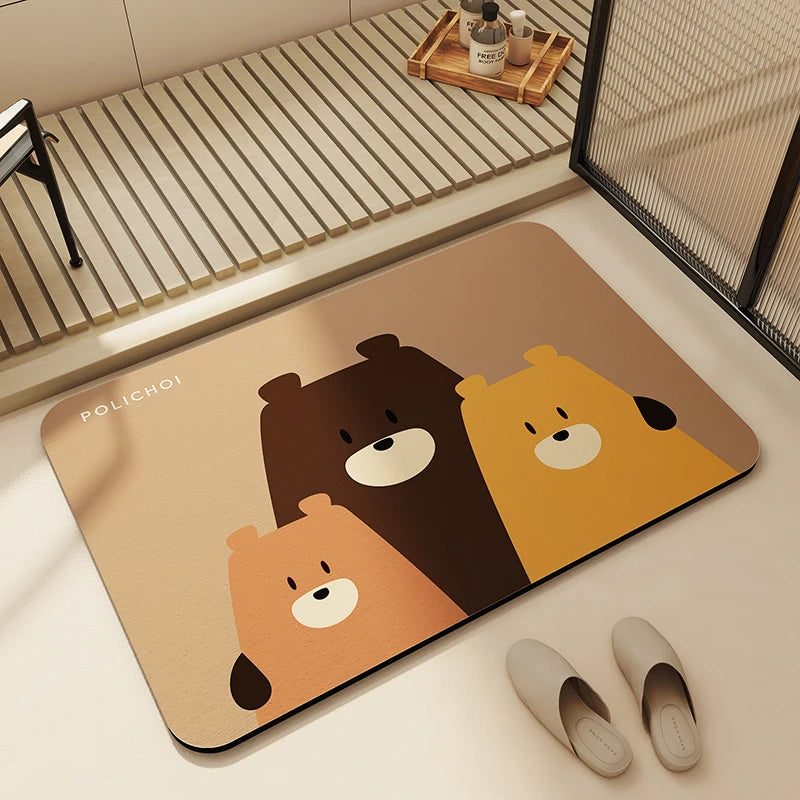A rectangular beige non-slip bathroom mat featuring three bear designs in brown, yellow, and orange.