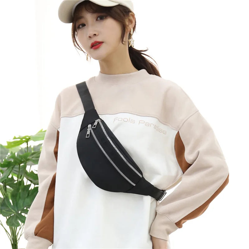A woman wearing a beige sweatshirt with a black nylon waist pack and brown accents.