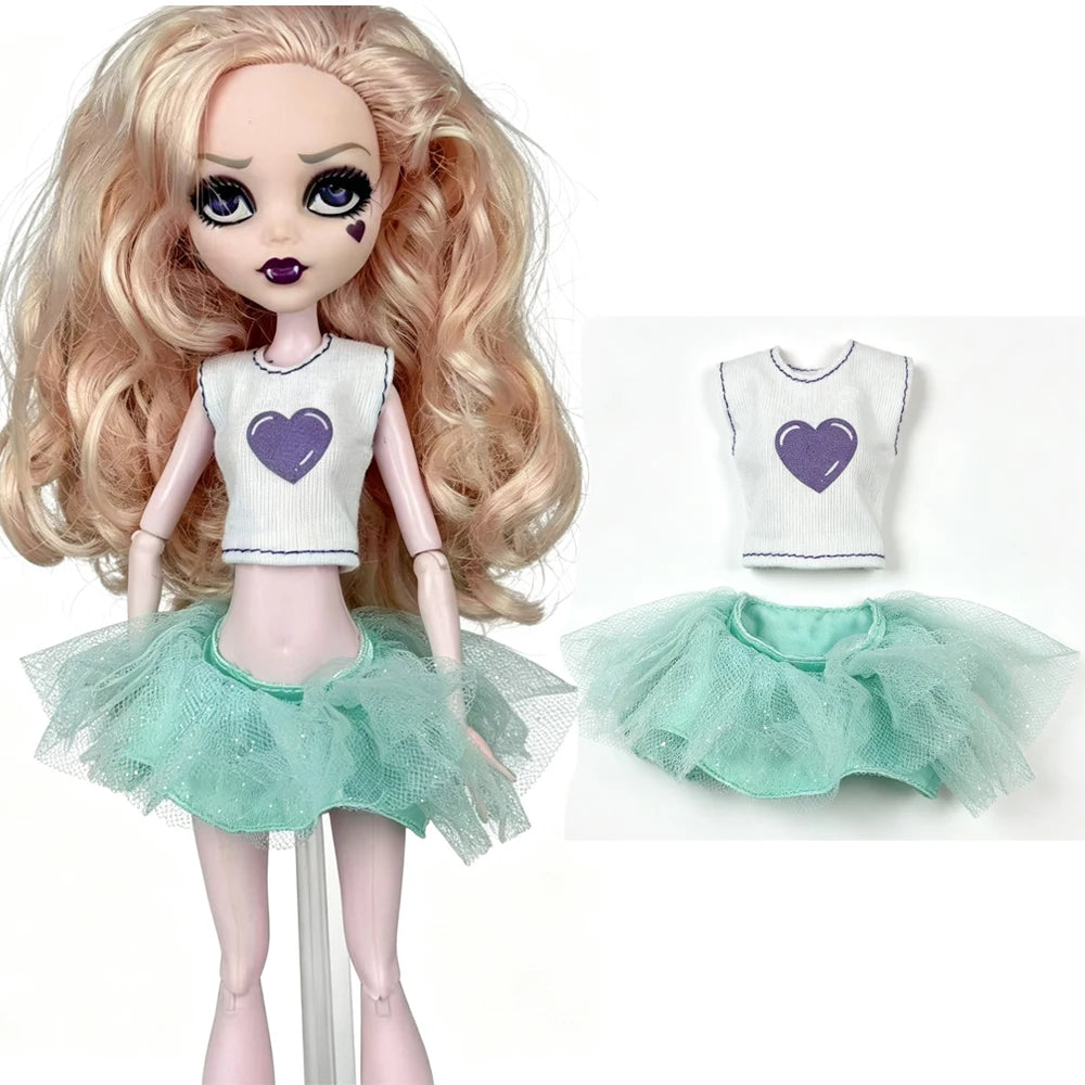 A fashion doll wearing a white top with a purple heart and a sheer mint green tutu skirt.