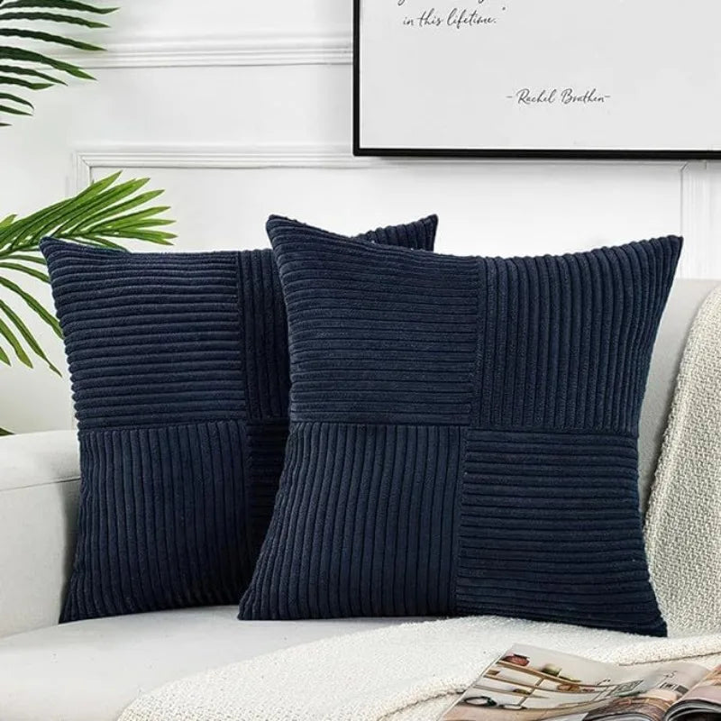 A set of two dark navy blue corduroy patchwork throw pillow covers with vertical ribbing on a white sofa.