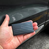 A hand holds a matte black 3D American flag car emblem set with ridged detailing against a dark car surface.