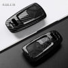 A black carbon fiber style key fob cover for an Audi, shown in a diagonal angle on a dark surface.