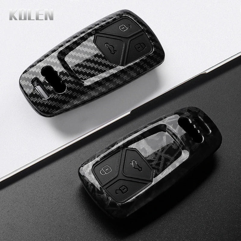A black carbon fiber style key fob cover for an Audi, shown in a diagonal angle on a dark surface.