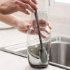 Hands are cleaning the inside of a glass bottle with a silicone brush to remove residue.