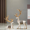 A set of two resin deer figurines, one with antlers and another standing, in white and gold tones.