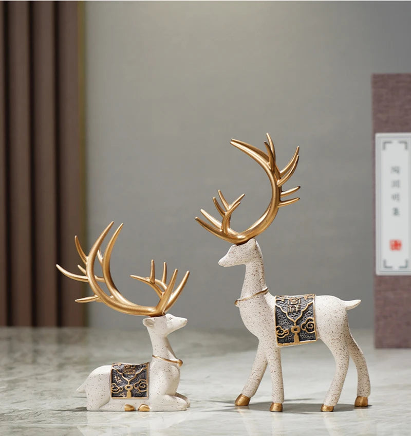 A set of two resin deer figurines, one with antlers and another standing, in white and gold tones.