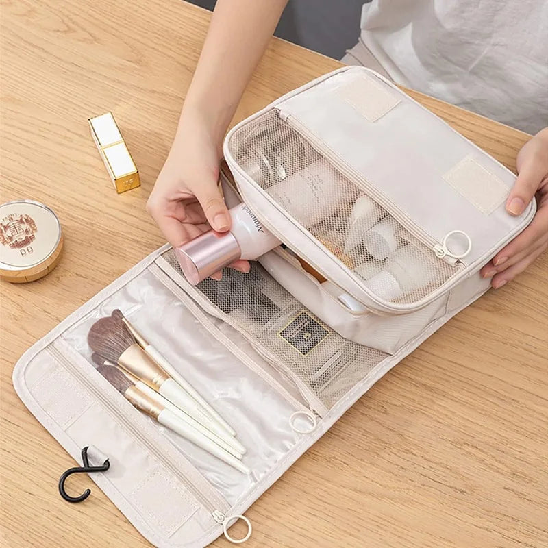 A light pink travel makeup bag with a mesh organizer and hanging hook is shown open on a wooden table.