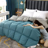 A woman is relaxing on a teal quilted comforter in a bedroom setting with dark blue curtains and a gold headboard.