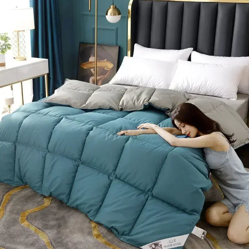 A woman is relaxing on a teal quilted comforter in a bedroom setting with dark blue curtains and a gold headboard.