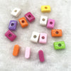 A collection of 10 mixed alphabet letter beads in various colors and shapes scattered on a white, fluffy surface.