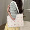 A woman is holding a white quilted laptop shoulder bag with pink bows and padded protection against a light-colored door.