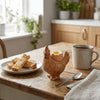 A ceramic chicken egg cup with a realistic yellow-brown chicken figure and an egg sitting on a wooden table.