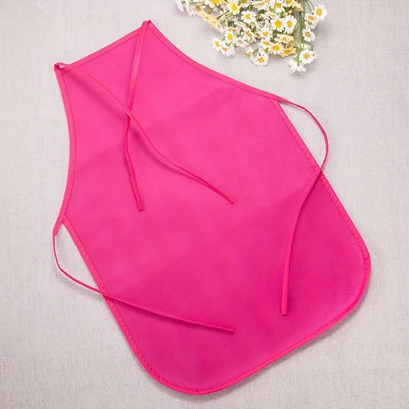 A bright pink non-woven fabric craft apron is displayed against a light background with a small bouquet of white flowers.