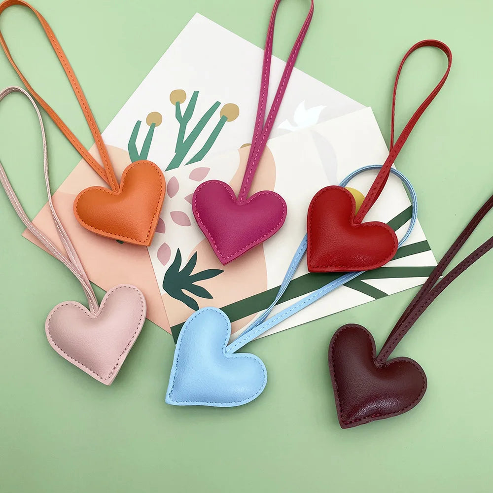 A collection of heart-shaped PU leather keychains in various colors, including peach, purple, red, blue, and brown.