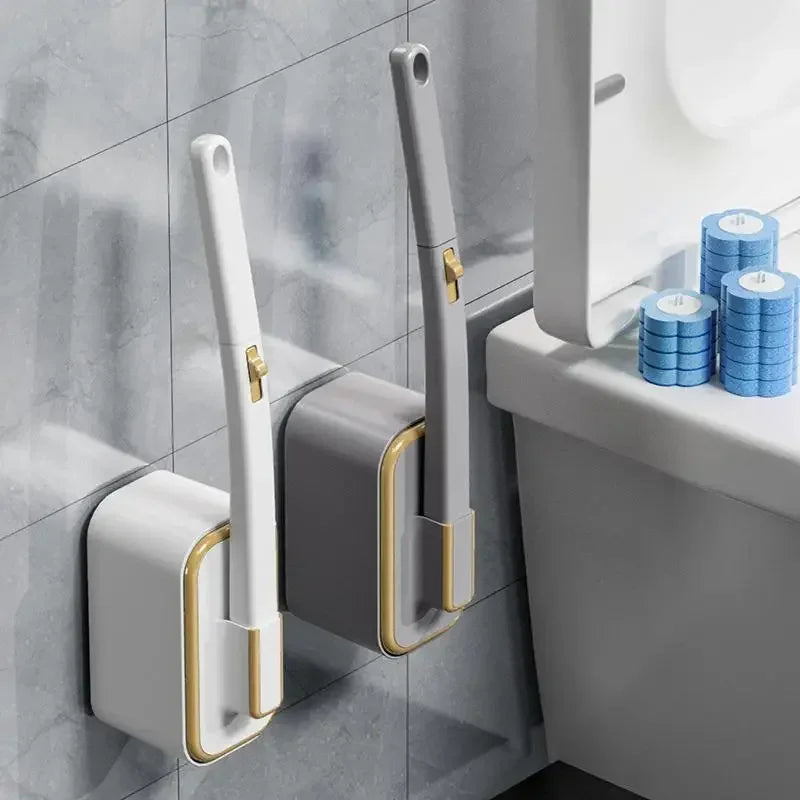 A white and gold disposable toilet cleaning brush with a handle is mounted on a gray wall.