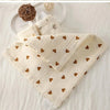 A stack of soft beige cotton gauze burp cloths with small brown heart patterns, resting on a white surface.
