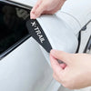 A hand is applying an X-TRAIL rain guard to the side mirror of a white car.