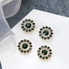 Five clusters of dark green and clear rhinestones shaped like flowers displayed on a white surface.