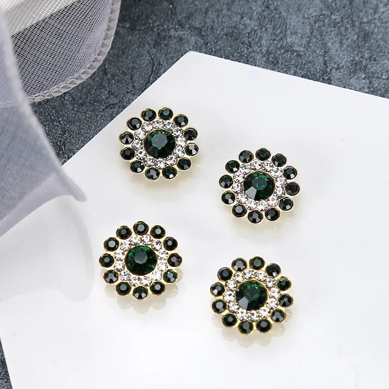 Five clusters of dark green and clear rhinestones shaped like flowers displayed on a white surface.