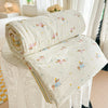 A cream-colored lightweight quilt with a pastoral print featuring small animals and flowers, rolled up on a white surface.