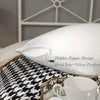 Un oreiller blanc avec un motif de fermeture éclair posé sur un tissu à motifs noir et blanc.
