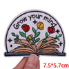 An embroidered patch featuring an open book with flowers and stars on a light pink background.