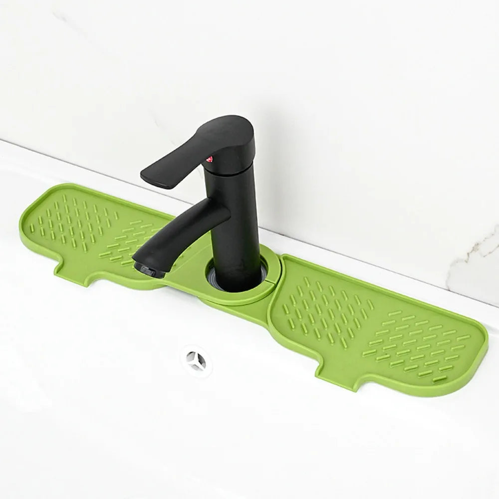 A black silicone faucet mat with a handle and splash guard is placed on a white countertop.