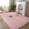 A fluffy pink Nordic furry accent rug placed on a light wood floor next to a white shelving unit.