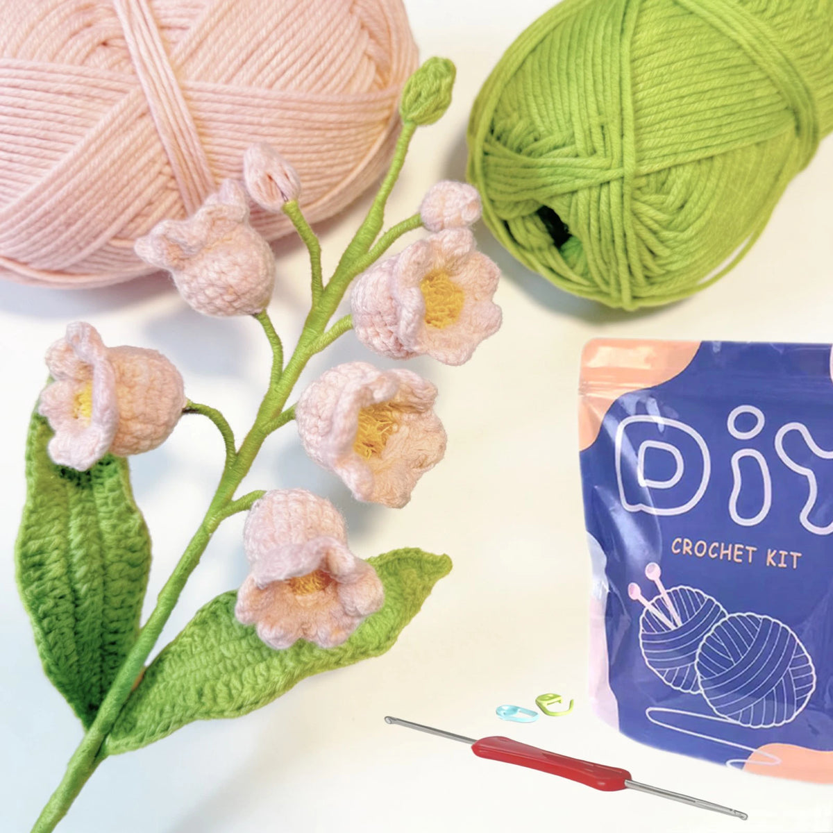 A crochet kit featuring pink and green yarn, a needle, and plant-like crocheted flowers on a green leaf.