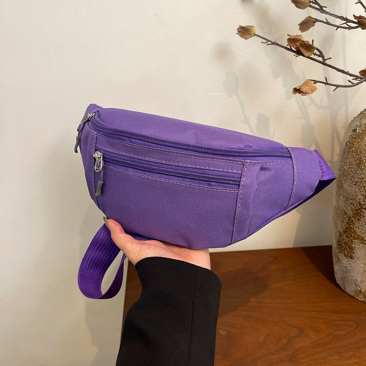 A purple nylon crossbody waist pack is held by a hand against a light background.