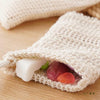 A natural sisal mesh bag is shown open, containing a white soap bar and pieces of fruit.
