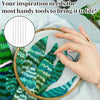 A hand holds a set of sewing needles over a green fabric featuring tropical leaf patterns.