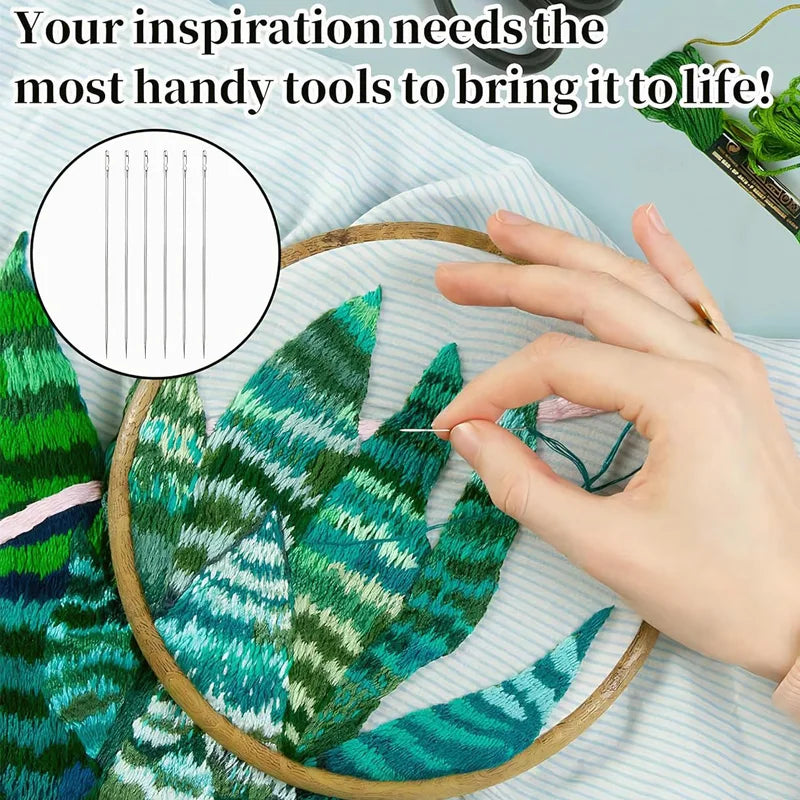 A hand holds a set of sewing needles over a green fabric featuring tropical leaf patterns.