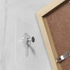 A silver self-adhesive wall hook is attached to a white wall next to a wooden picture frame.