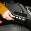 A hand is opening a black coin storage box with multiple slots inside, set against a dark car interior background.