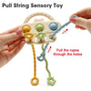 A hand is pulling a silicone teether toy with pull strings through holes, showing various colored textures.