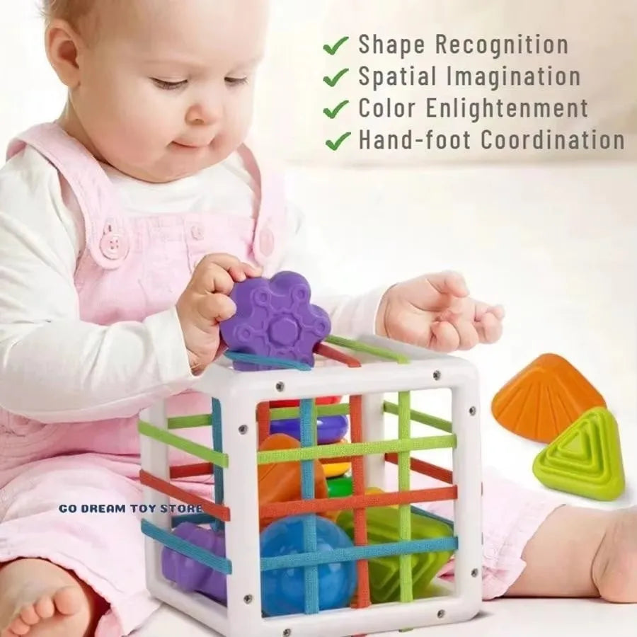 A baby is playing with a white plastic toy that features various colored shapes and balls for sensory development.