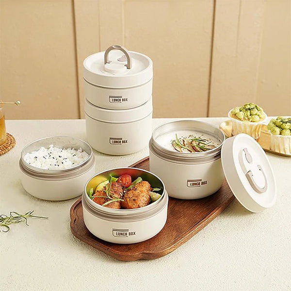 A set of three stackable white insulated lunch boxes with lids and a wooden serving board.