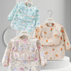 A light pink and green floral waterproof long sleeve feeding bib with a catch pocket displayed on a hanger.