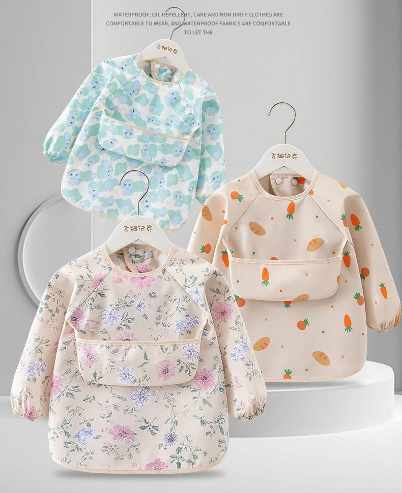 A light pink and green floral waterproof long sleeve feeding bib with a catch pocket displayed on a hanger.