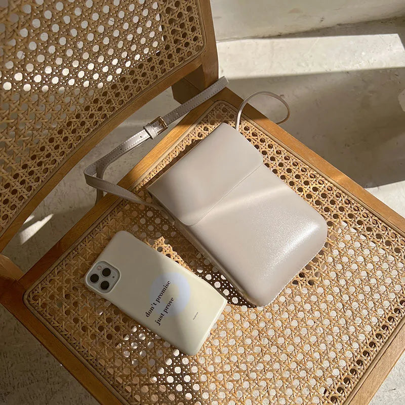 A light beige vintage PU leather crossbody shoulder bag resting on a woven wooden tray.