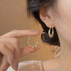 Close-up of a hand wearing twisted zircon hoop earrings in a gold finish