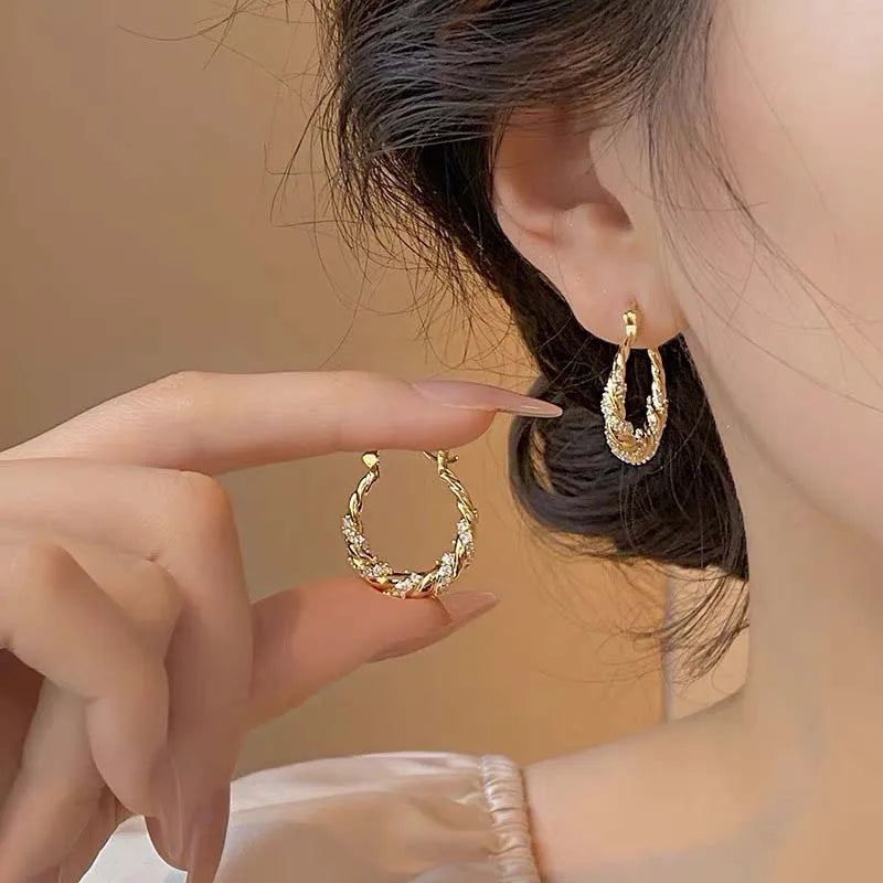 Close-up of a hand wearing twisted zircon hoop earrings in a gold finish